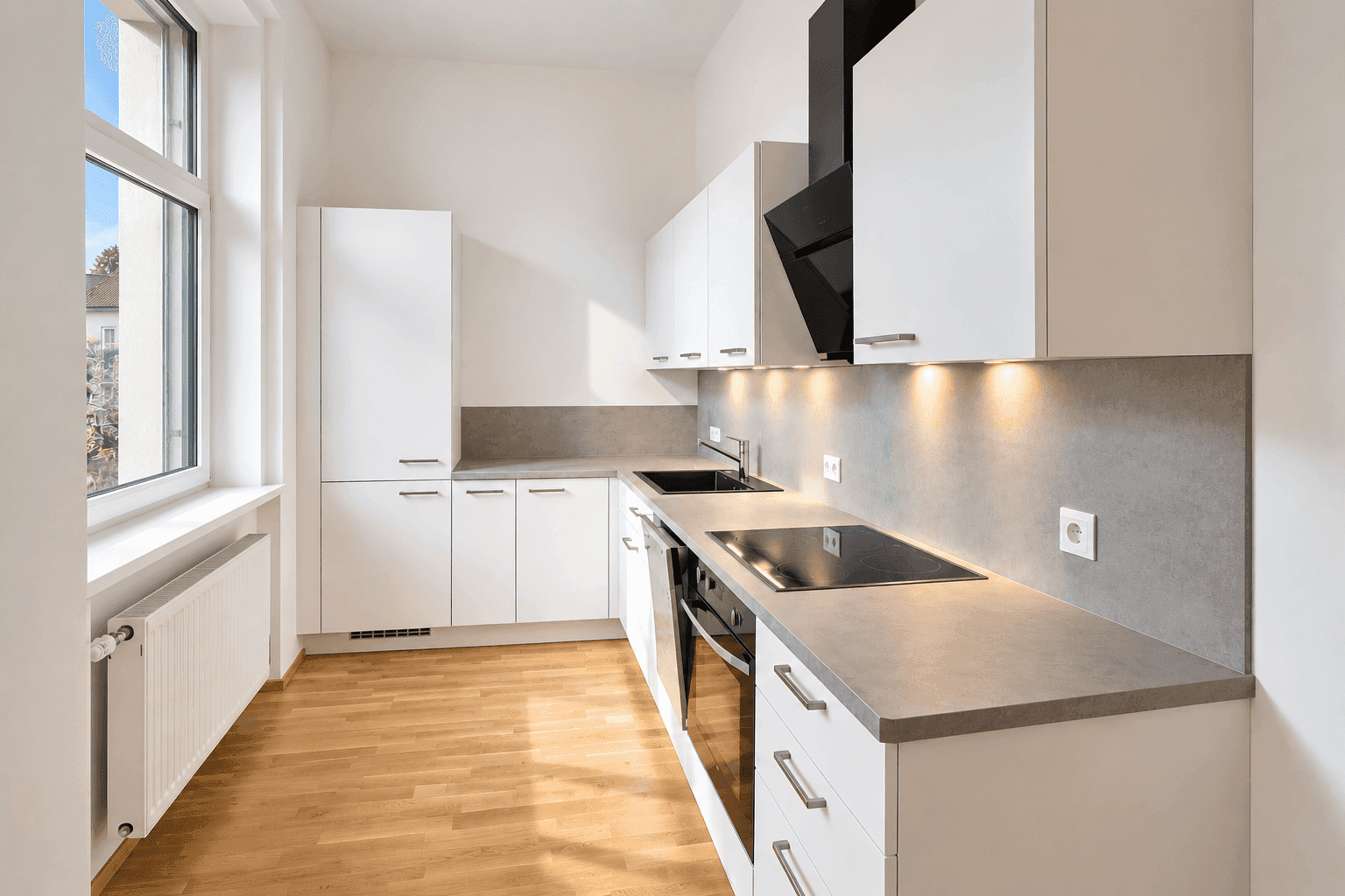 Moderne Einbauküche mit weißen Schränken, Induktionskochfeld und hellem Parkettboden.