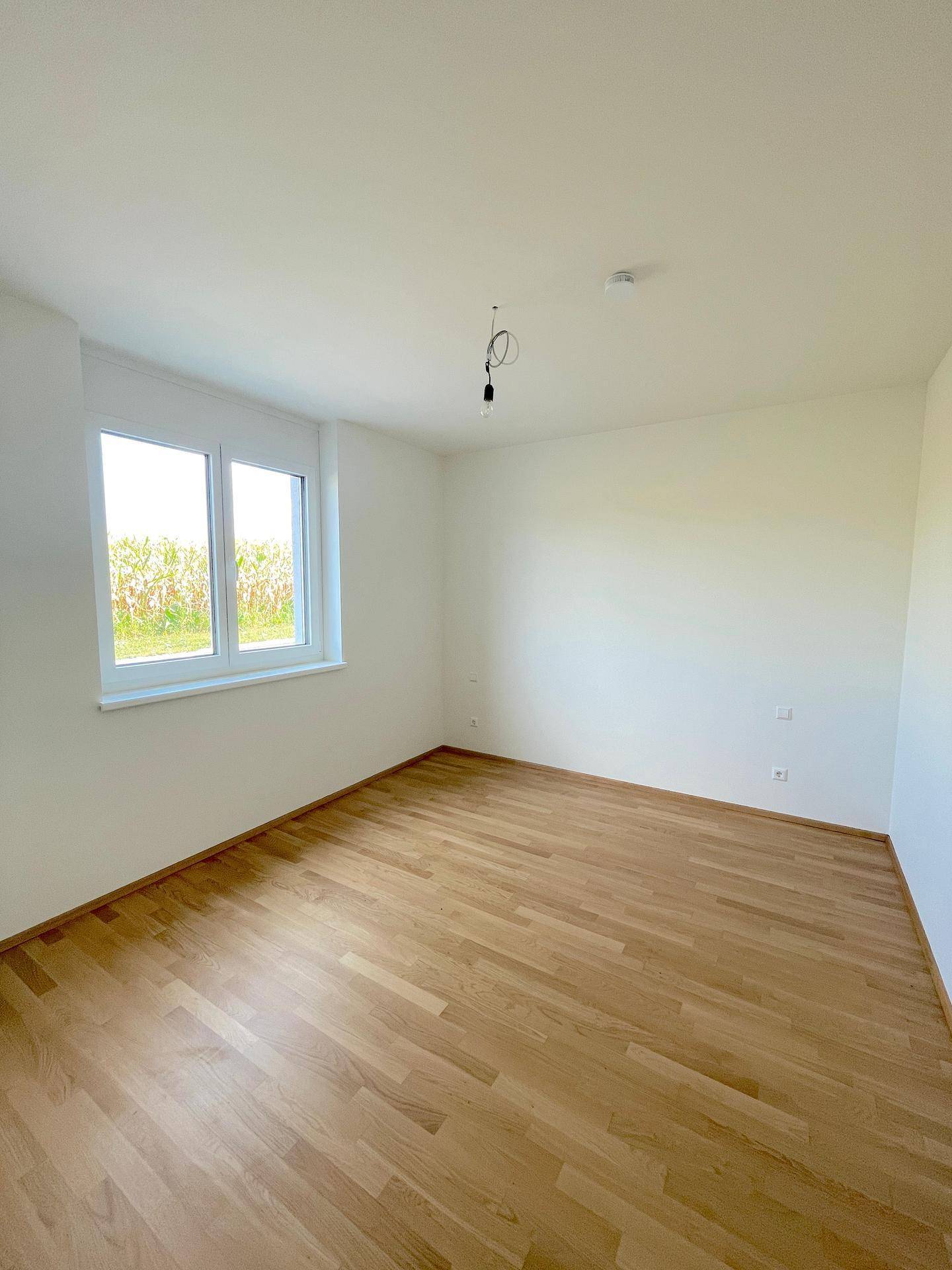 Helles Schlafzimmer mit Holzboden und Blick auf die grüne Landschaft durch das Fenster.