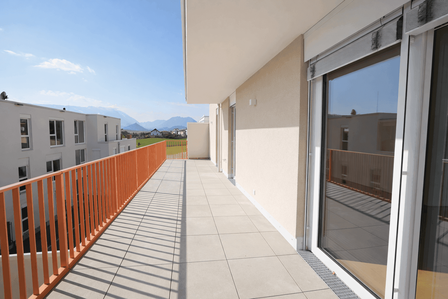 Lange, geflieste Terrasse mit modernem orangefarbenem Geländer und Zugang zu den Innenräumen.