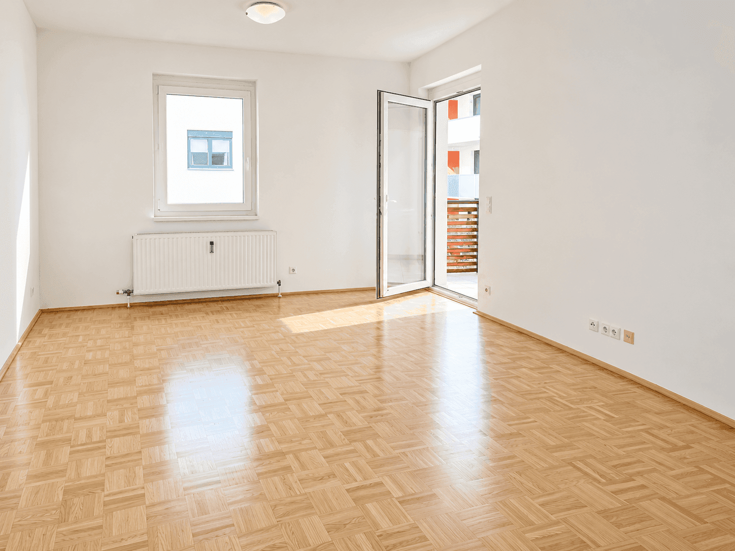 Geräumiges, helles Wohnzimmer mit Parkettboden und Zugang zu einem Balkon.