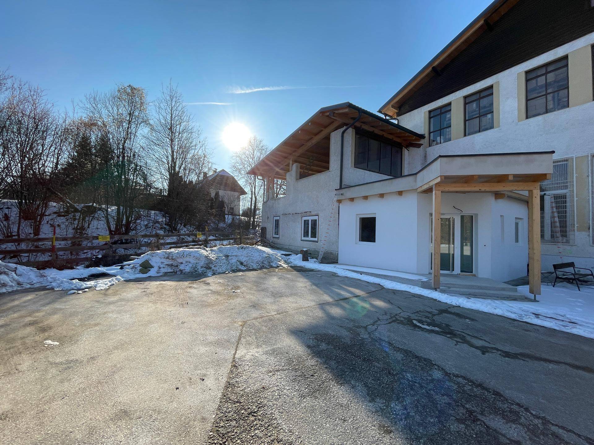 Außenansicht eines modernen Gebäudes mit weißer Fassade und Holzelementen, umgeben von Schnee im Winter.