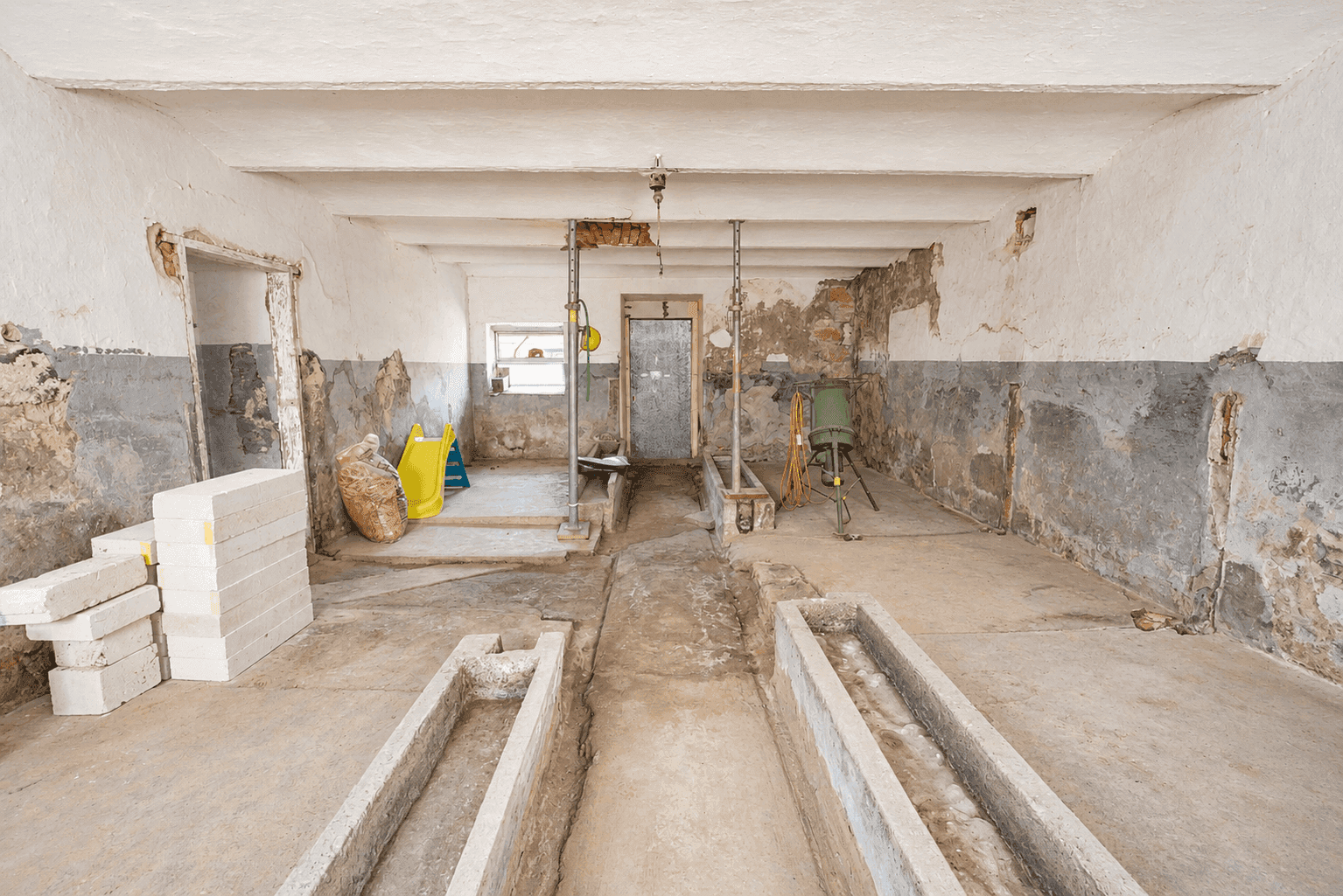 Rustikaler Kellerraum mit Betonboden und alten Trögen, geeignet für verschiedene Nutzungsmöglichkeiten.