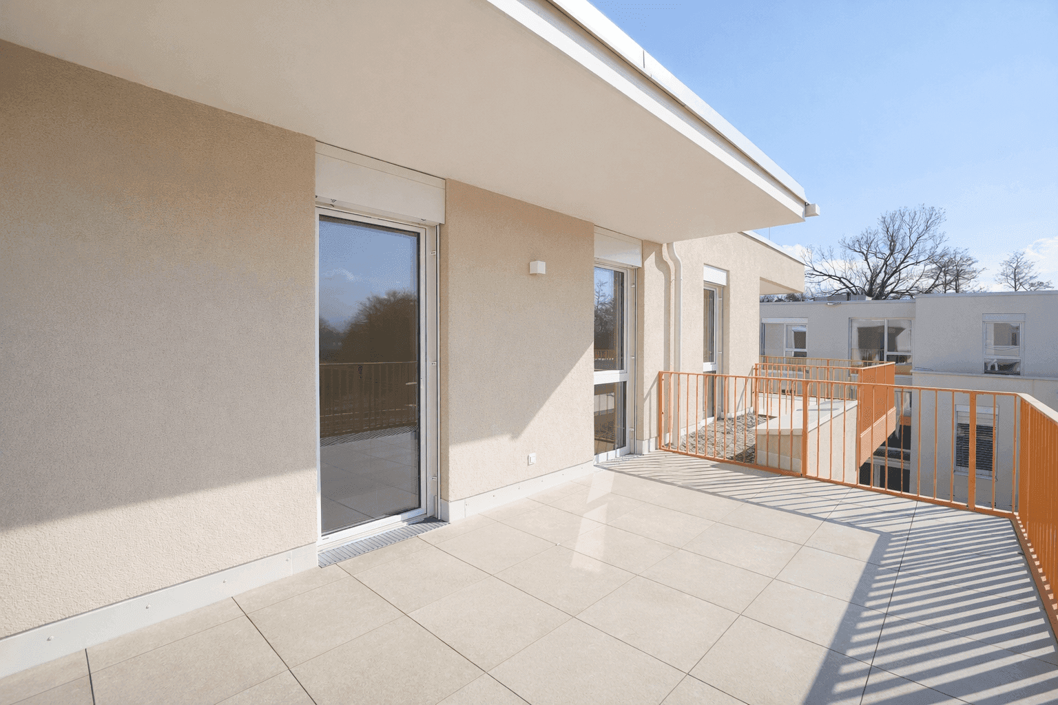 Geräumige, geflieste Terrasse mit moderner Brüstung und Rollläden an den Fenstern.
