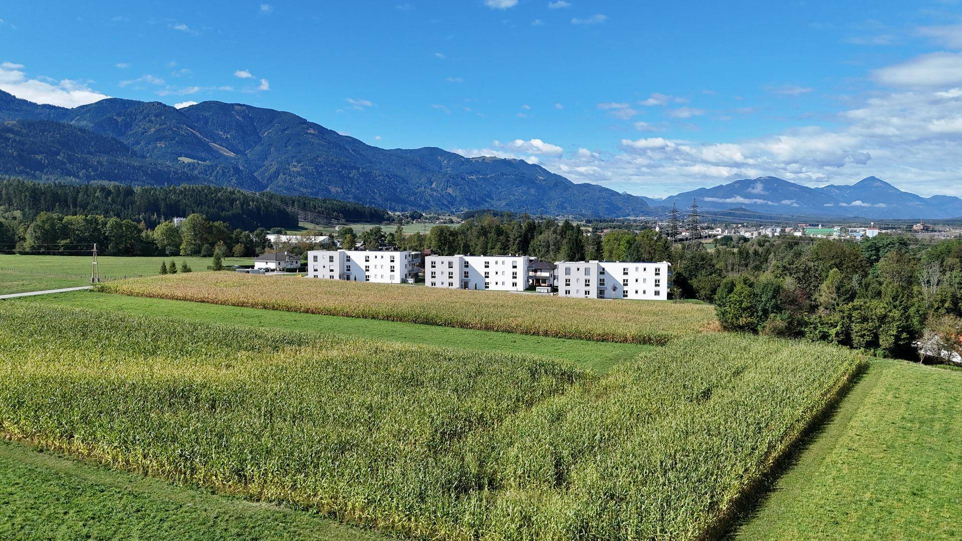 Reihe von modernen Wohngebäuden in einer idyllischen Landschaft mit weiten Feldern und Bergen.