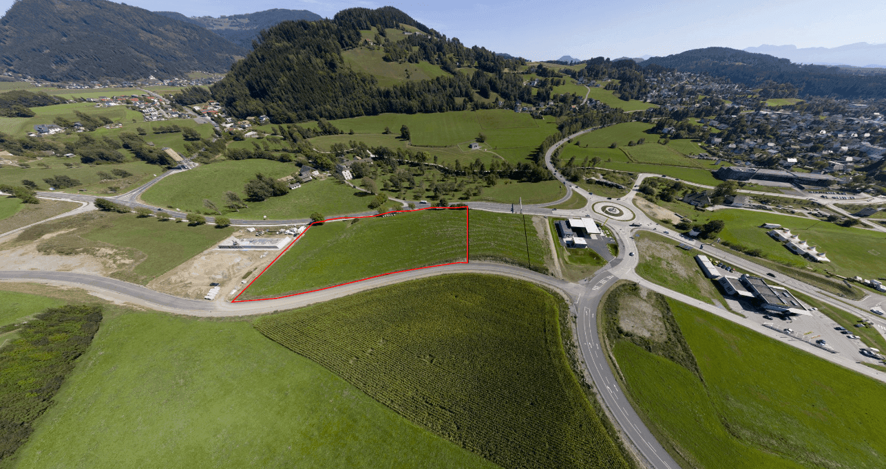 Luftaufnahme eines Baugrundstücks, rot umrandet, umgeben von Straßen und ländlicher Umgebung.