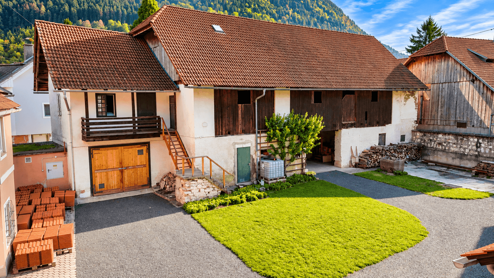 Historisches Bauernhaus mit Holzelementen und großem Hof, umgeben von grüner Landschaft und Bergen.