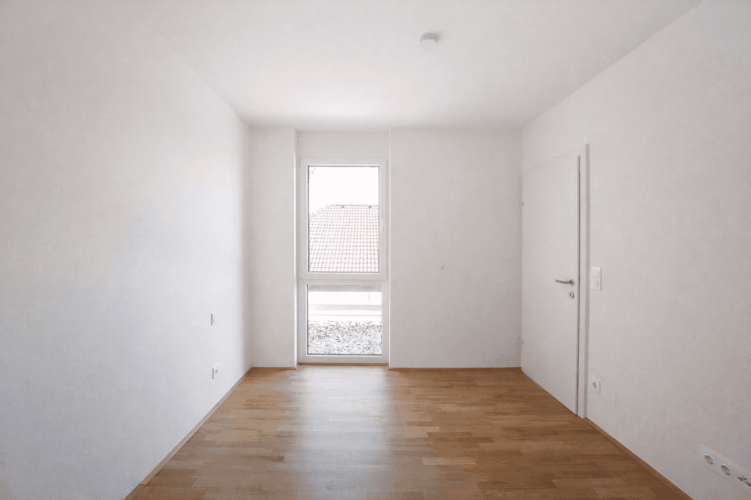 Helles Schlafzimmer mit Parkettboden und einem Fenster, das viel Tageslicht hereinlässt.