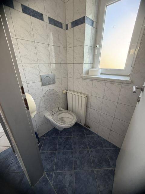 Toilette mit Fenster, Heizkörper und blau-weißen Fliesen, in einem sauberen Zustand.