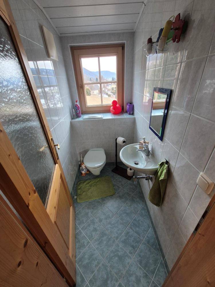 Kleines WC mit Waschbecken, Toilette und Fenster, hell durch natürliches Licht.
