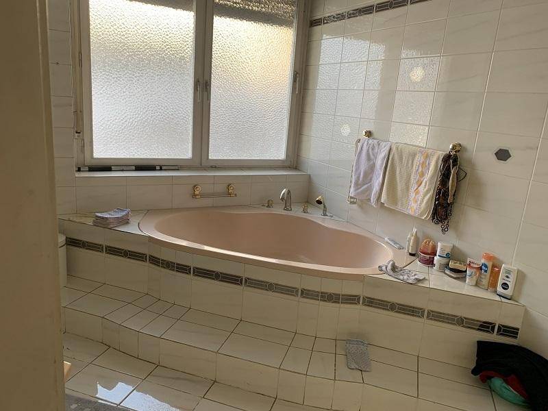 Badezimmer mit Eckbadewanne, Fenster und hellen Wandfliesen.