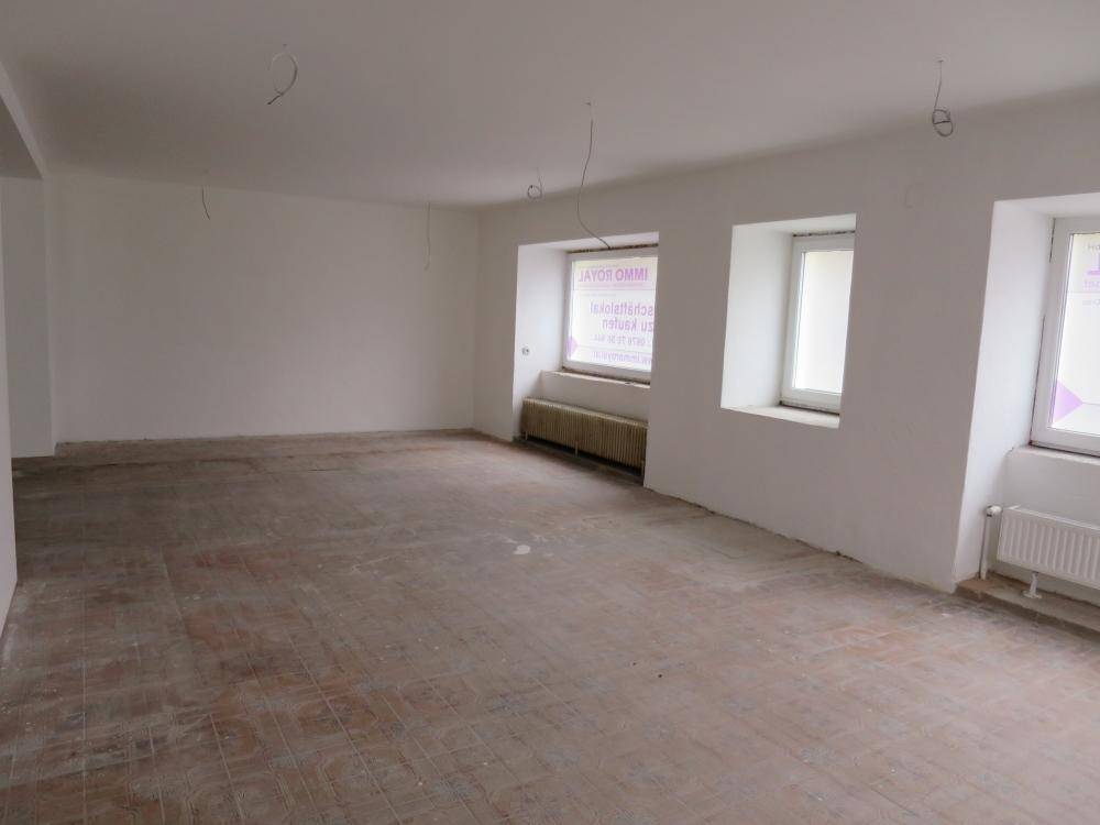Heller, leerer Raum mit Fliesenboden, mehreren Fenstern und Heizkörpern, ideal für Renovierungsprojekte.