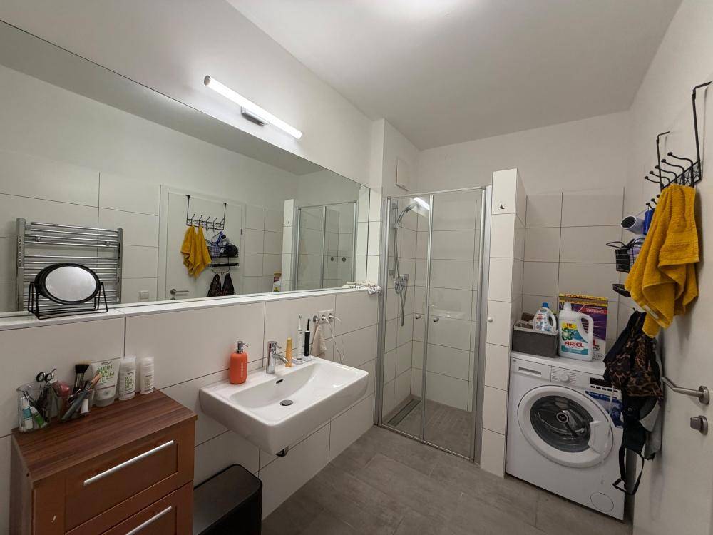 Funktionales Badezimmer mit Duschkabine, Waschbecken, Waschmaschine und beheiztem Handtuchhalter.
