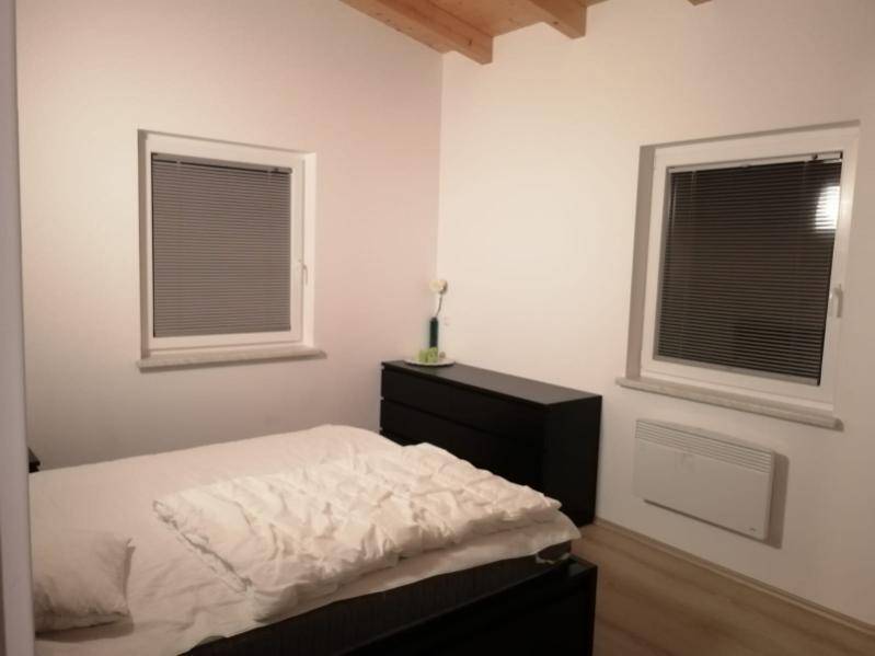 Schlafzimmer mit Doppelbett, zwei Fenstern und dunkler Kommode.