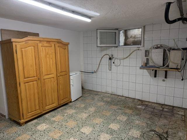 Kellerraum mit Holzschrank, Kühlschrank und gefliesten Wänden, für Lagerzwecke genutzt.