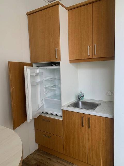 Kompakte Küchenzeile mit Holzschränken, Spüle und integriertem Kühlschrank, praktisch und funktional für den Arbeitsalltag.