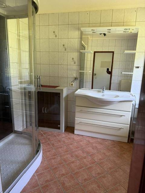 Badezimmer mit moderner Duschkabine, Waschtisch und Spiegel, sowie braunen Fliesen.