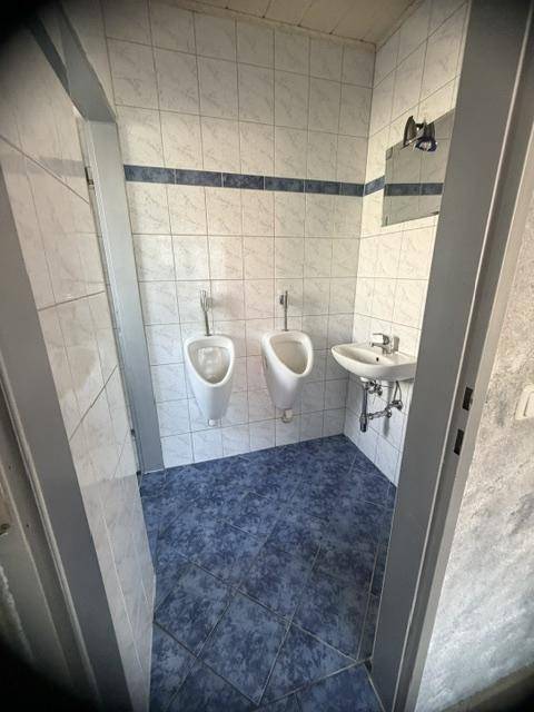 Herren-WC mit zwei Urinalen, Waschbecken und blau-weißen Fliesen, sauber und funktional.