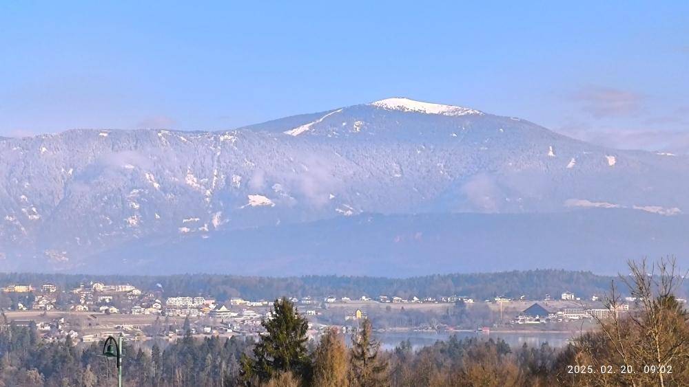 Weitläufiger Blick auf schneebedeckte Berge und eine darunterliegende Siedlung mit See.