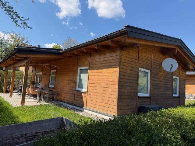 Holzhaus mit Satellitenschüssel, Rasenfläche und überdachtem Terrassenbereich.