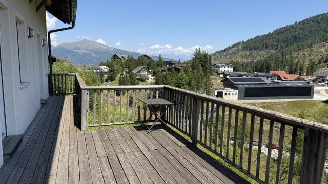 Geräumiger Holzbalkon mit kleinem Tisch und Panoramablick auf die Berge und das Tal.