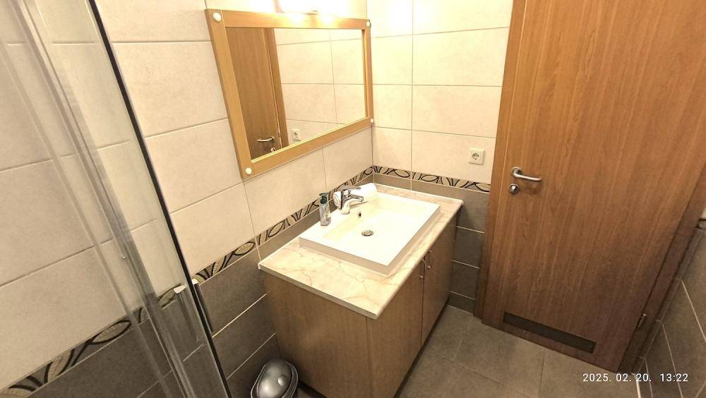 Badezimmer mit Waschtisch, Spiegel und Duschkabine, funktional und hell gefliest.