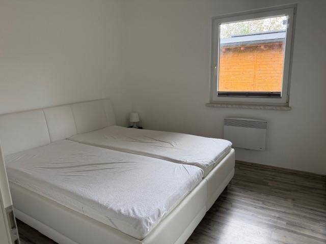 Schlafzimmer mit Doppelbett, Laminatboden und Fenster mit Blick nach draußen.
