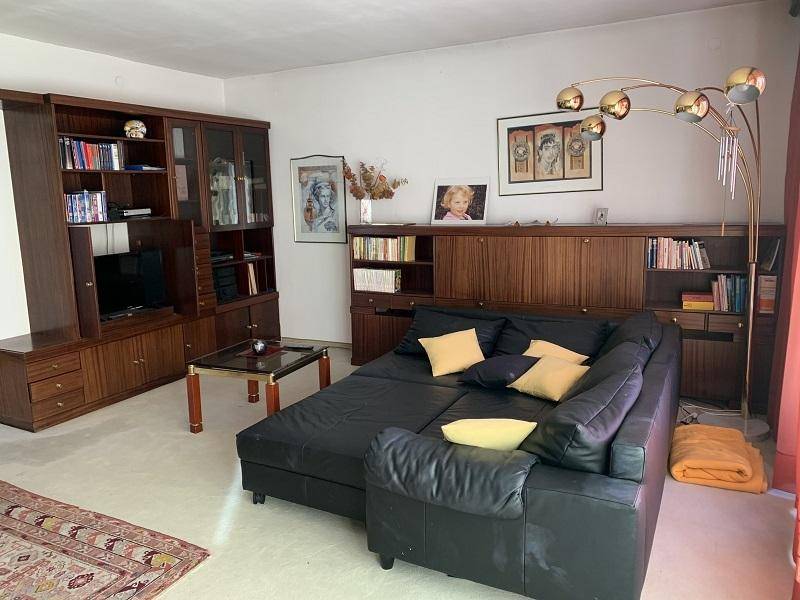 Wohnzimmer mit großem Ledersofa, Bücherregalen und Teppichboden.
