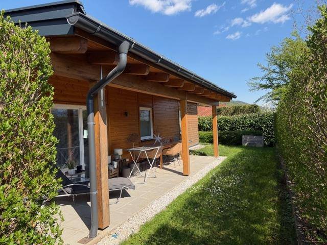 Seitliche Terrasse mit Gartenmöbeln, Rasenfläche und Hecke.