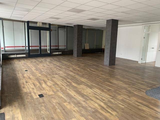 Geräumiger, leerer Geschäftsraum mit Holzoptik-Laminatboden und großen Fenstern zur Straße, die viel Licht hereinlassen.
