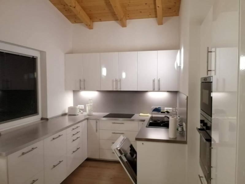 Moderne Küche mit weißen Schränken, Edelstahl-Arbeitsplatten und Holzbalkendecke.