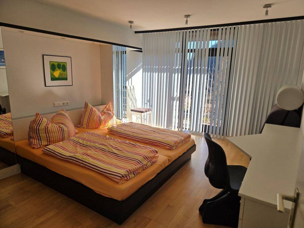 Helles Schlafzimmer mit zwei Einzelbetten, Holzboden und großen Fenstern mit Jalousien.