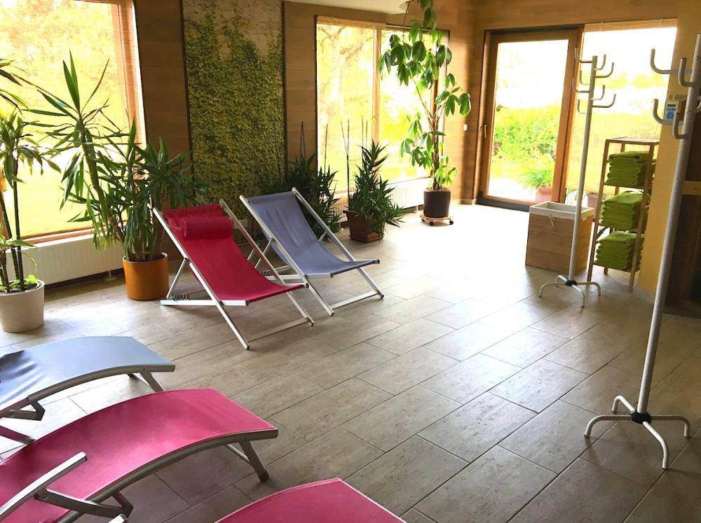 Heller Wellnessbereich mit vielen Pflanzen, Liegestühlen und Zugang zum Außenbereich.