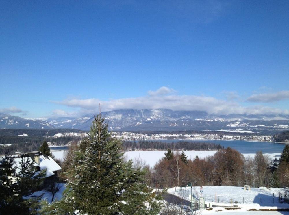 Winterlicher Panoramablick auf einen zugefrorenen See und schneebedeckte Berge unter blauem Himmel.