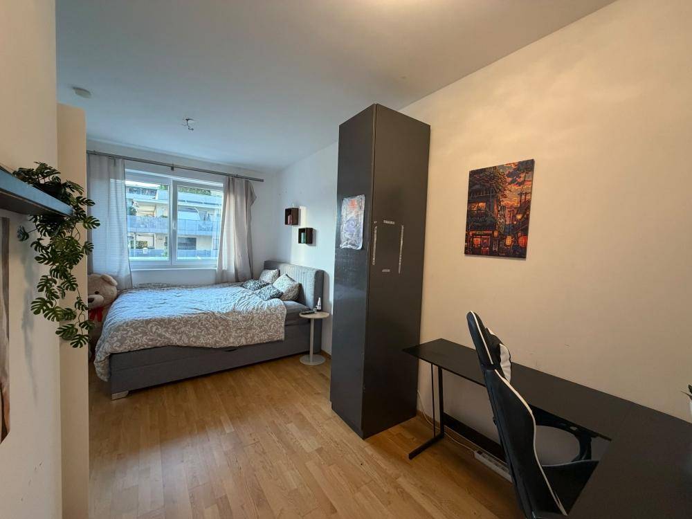 Helles Schlafzimmer mit Bett, Fenster und einem funktionalen Schreibtischbereich.