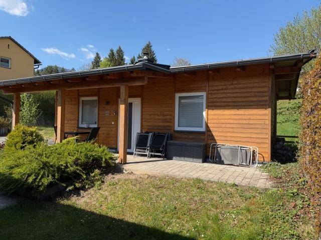 Holzhaus mit kleiner gepflasterter Terrasse und Gartenmöbeln im Freien.
