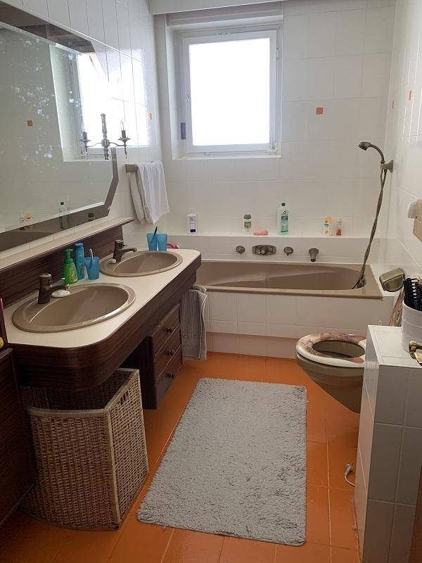Badezimmer mit Doppelwaschbecken, Badewanne und orangefarbenem Fliesenboden.