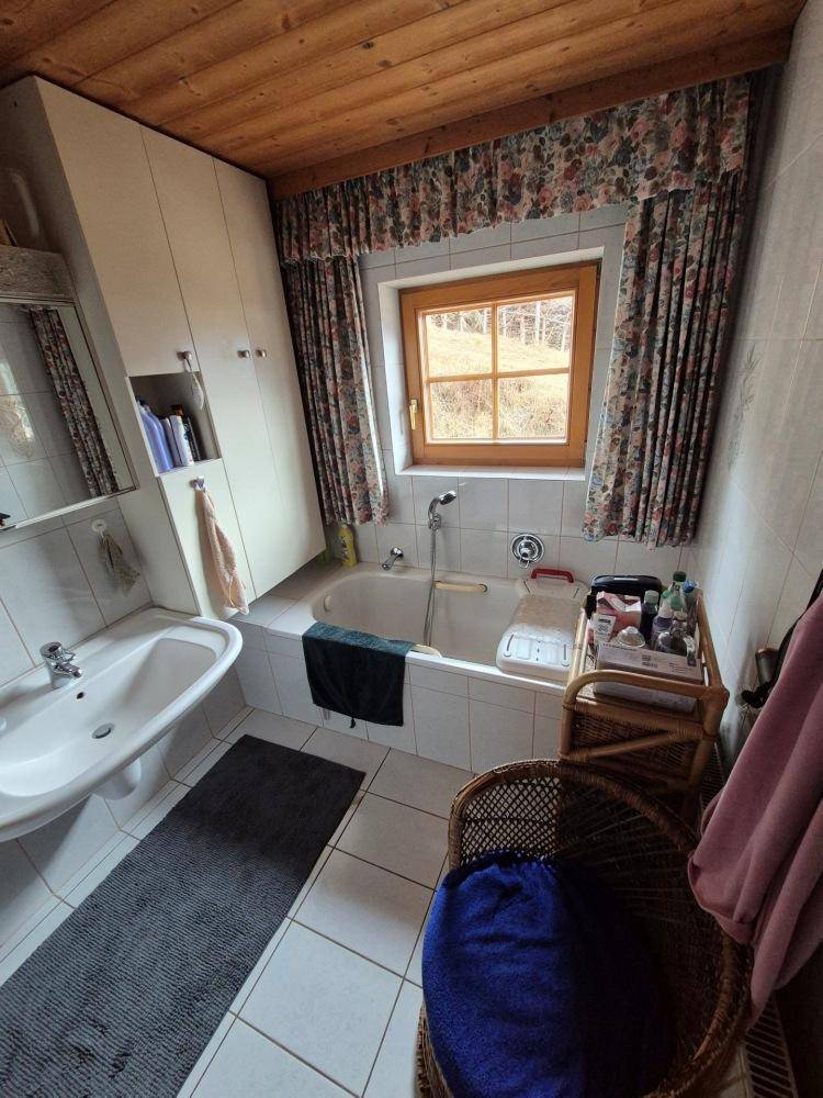 Badezimmer mit Badewanne, Waschbecken und Fenster, dekoriert mit floralen Vorhängen.