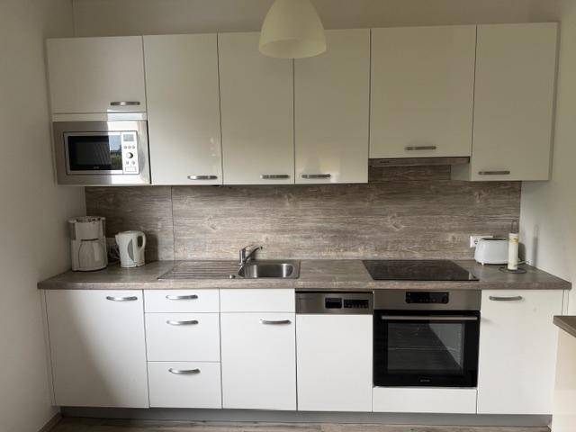 Moderne Einbauküche mit weißen Schränken, Mikrowelle und Induktionskochfeld.