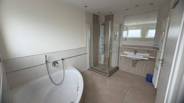 Modernes Badezimmer mit Badewanne, Duschkabine, Einzelwaschbecken und Handtuchheizkörper.