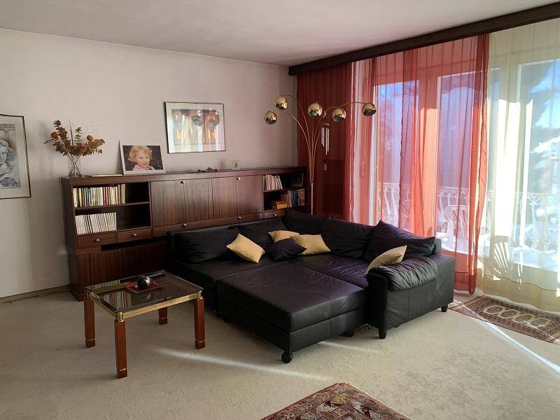 Gemütliches Wohnzimmer mit schwarzem Ledersofa, Holzregalen und Teppichboden.