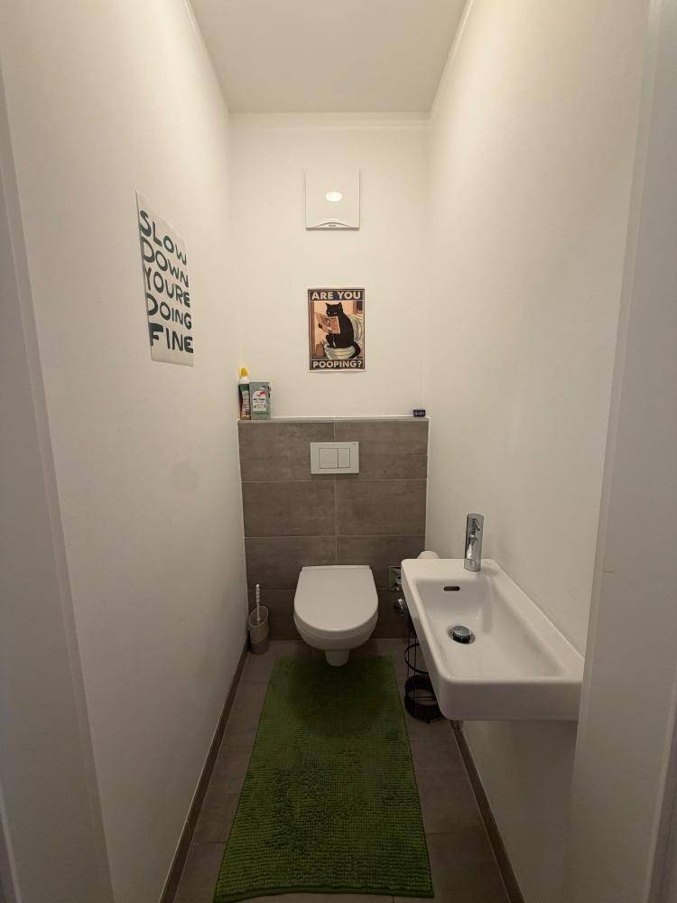 Modernes Gäste-WC mit wandhängender Toilette, kleinem Waschbecken und Fliesenboden.