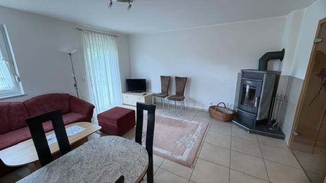 Heller Wohnbereich mit Kaminofen, rotem Sofa und Esstisch, ideal für gesellige Abende.