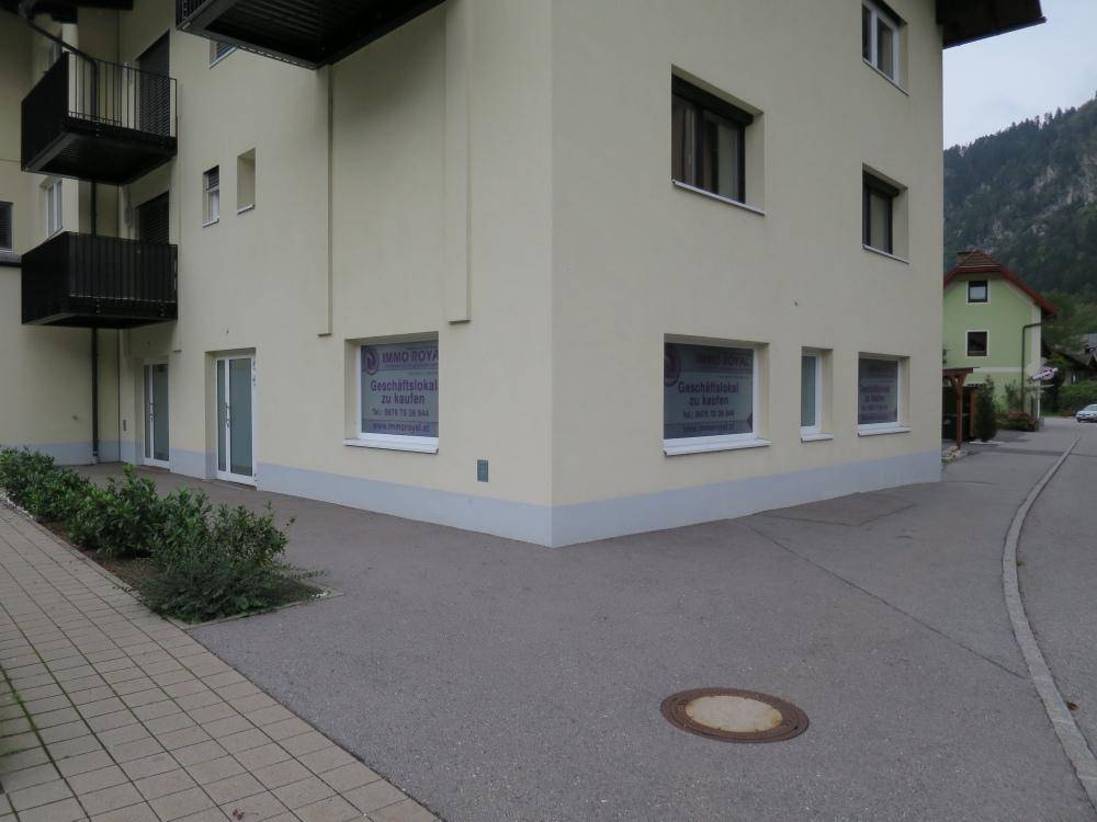 Eckansicht des Gebäudes mit Werbefenstern und angrenzender Straße, eingebettet in die Umgebung.