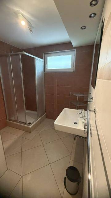 Modernes Badezimmer mit Duschkabine, Waschbecken und Fenster für natürliche Belüftung.