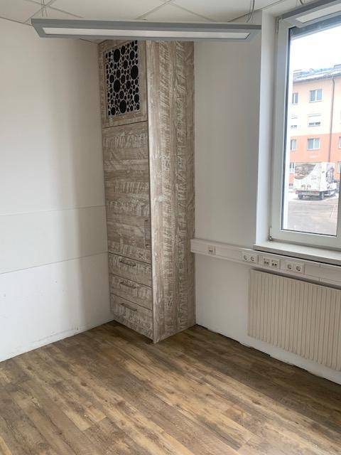 Ecke eines Raumes mit einem hohen Holzschrank und einem Fenster, das Tageslicht hereinlässt und Stauraum bietet.