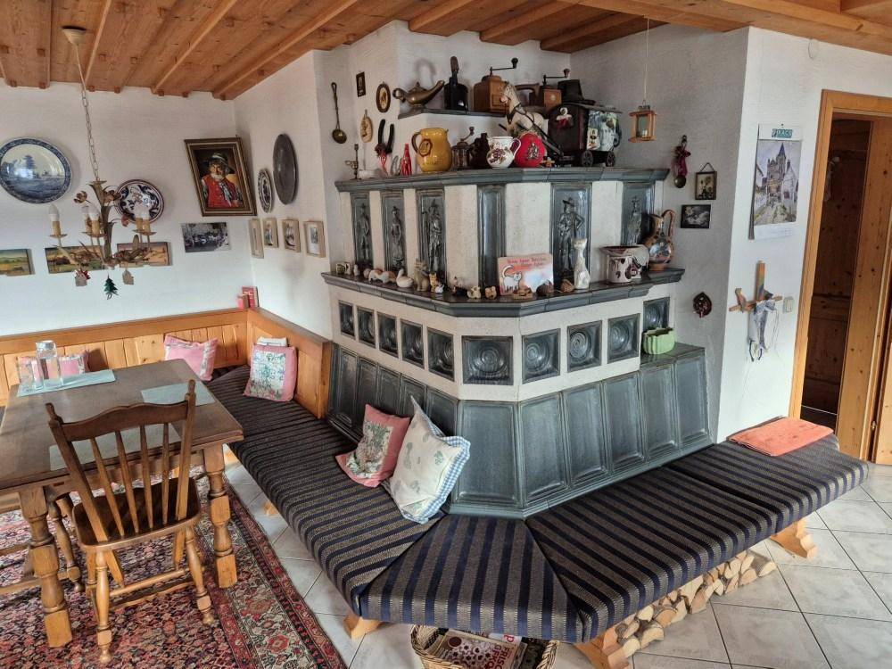 Traditioneller Wohn-Essbereich mit einem großen Kachelofen, Holzbänken und rustikalem Charme.