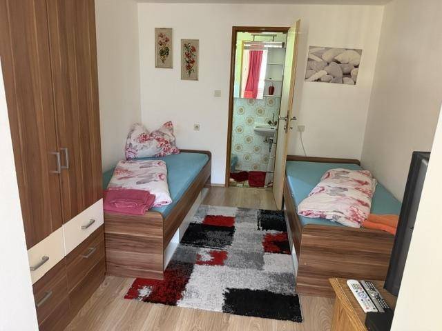Schlafzimmer mit zwei Einzelbetten, Kleiderschrank und Zugang zu einem kleinen Badezimmer.