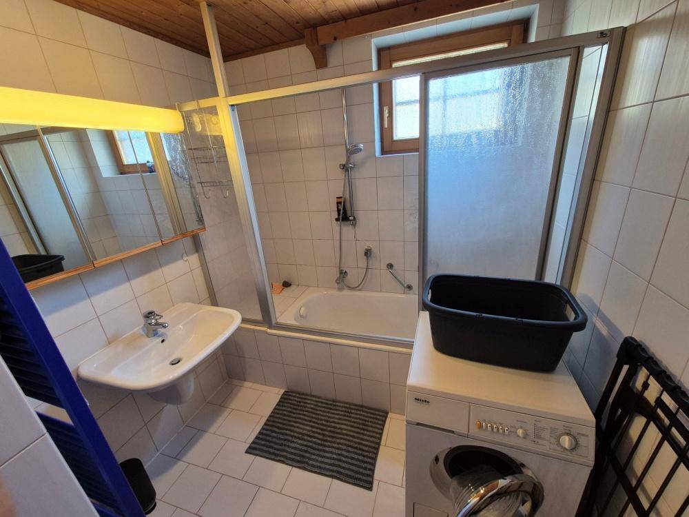 Badezimmer mit Badewanne, Duschabtrennung, Waschbecken und einer Waschmaschine, funktional eingerichtet.