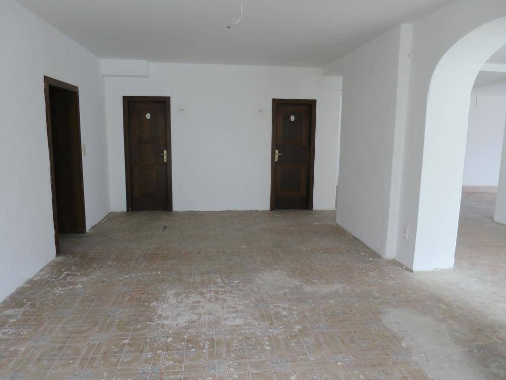 Geräumiger, leerer Raum mit Fliesenboden und mehreren Türen, ideal für individuelle Nutzung und Ausbau.