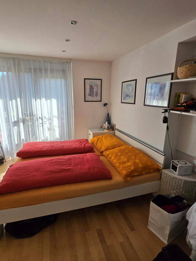 Helles Schlafzimmer mit Doppelbett, Holzboden und Zugang zu einem Balkon.